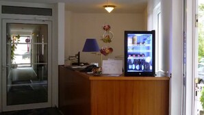 Un mostrador de recepción con un refrigerador que exhibe bebidas, una lámpara de escritorio y una ventana con vistas al exterior.