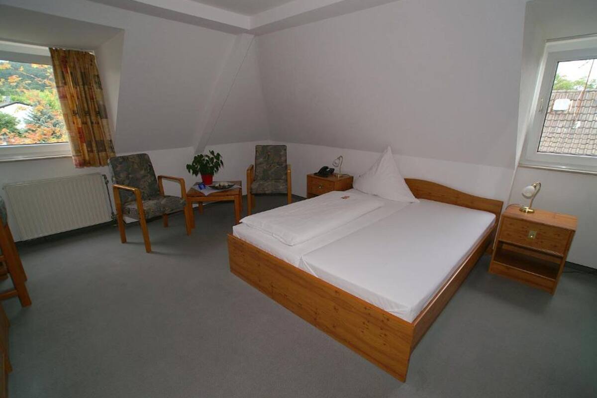 Een slaapkamer met een houten bed, twee stoelen, een klein tafeltje en een nachtkastje.