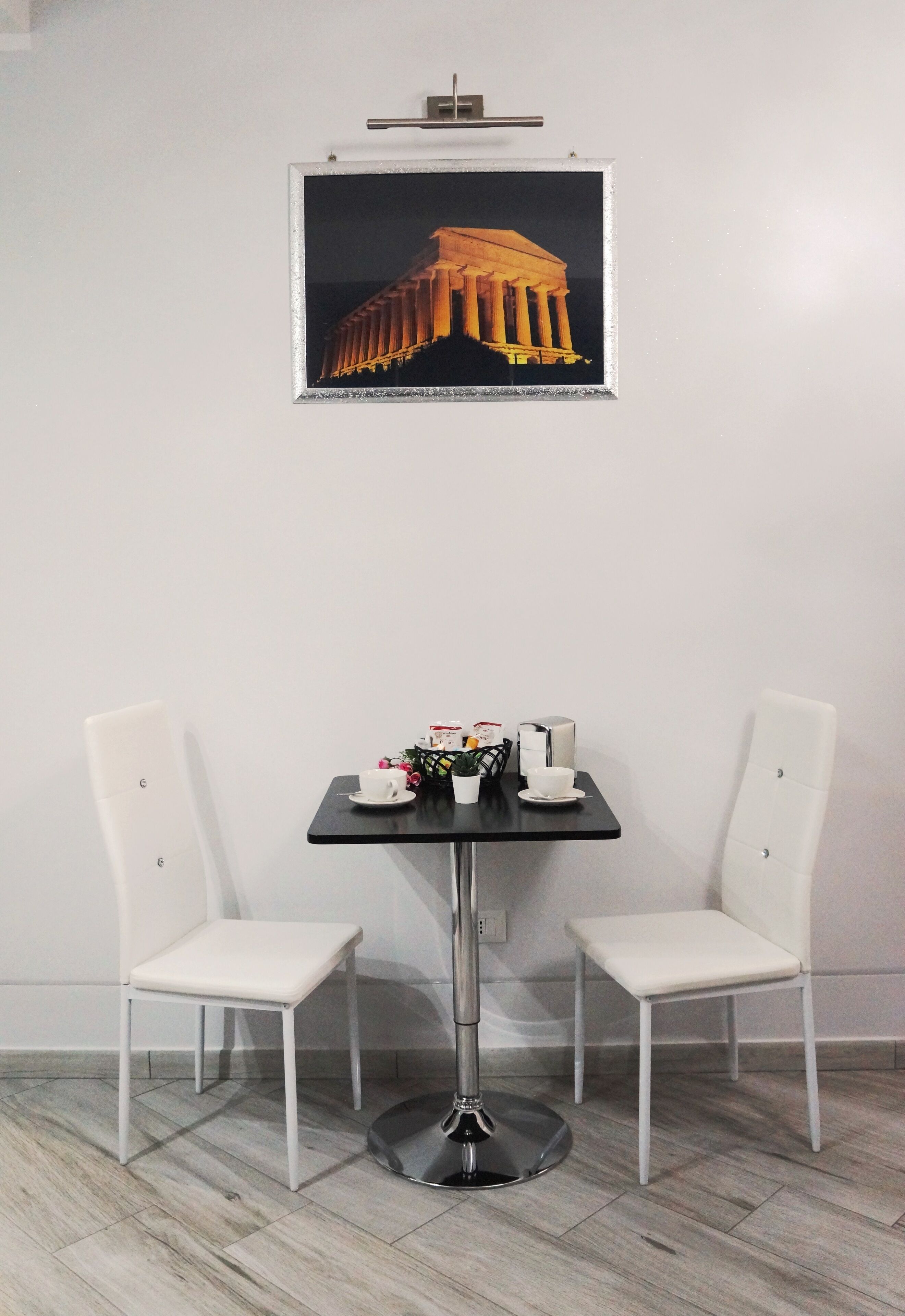 A modern room with a black table, two white chairs, a framed picture of a building, and a small potted plant.
