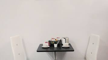 A modern room with a black table, two white chairs, a framed picture of a building, and a small potted plant.