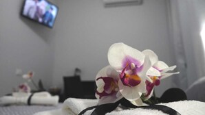 A hotel room with a bed, a TV mounted on the wall, and a bouquet of orchids on the bed. - B&B Agrigento da Tony Palermo (Agrigento)
