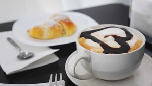 A cup of coffee with chocolate syrup on a saucer, a pastry on a plate, a spoon, and a fork on a table. - B&B Agrigento da Tony Palermo (Agrigento)