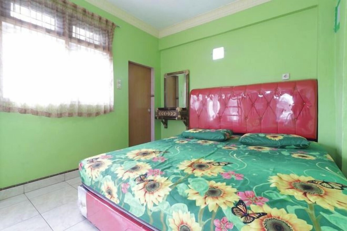 A bedroom with a floral bedspread, a red headboard, and a window with a curtain.