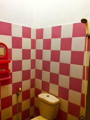 A small bathroom with a red and white checkered wall, a toilet, and a shower area. - Homestay Badak (Makassar)