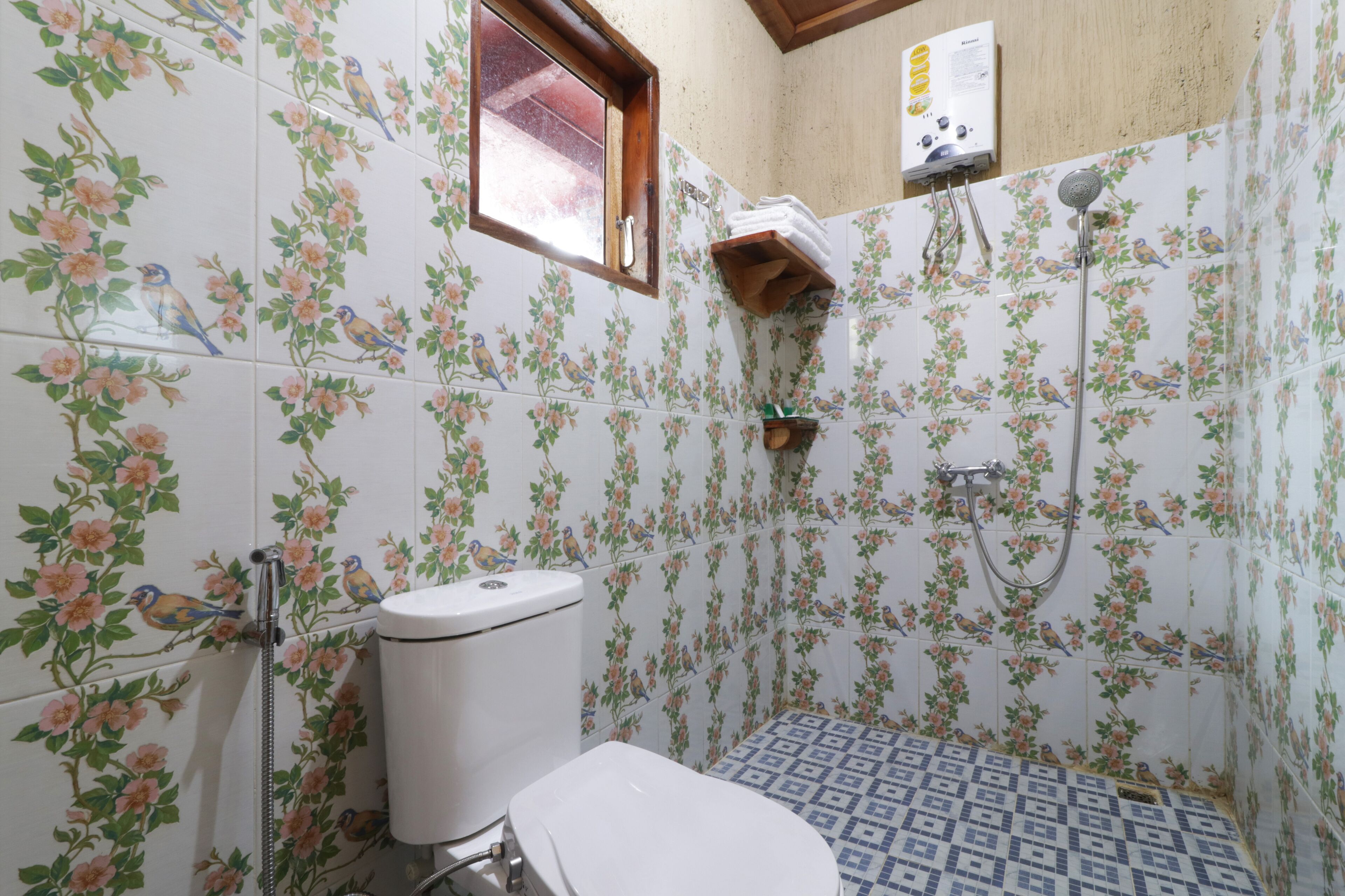A bathroom with floral tiles, a toilet, a shower, and a window.