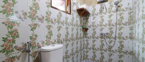 A bathroom with floral tiles, a toilet, a shower, and a window.