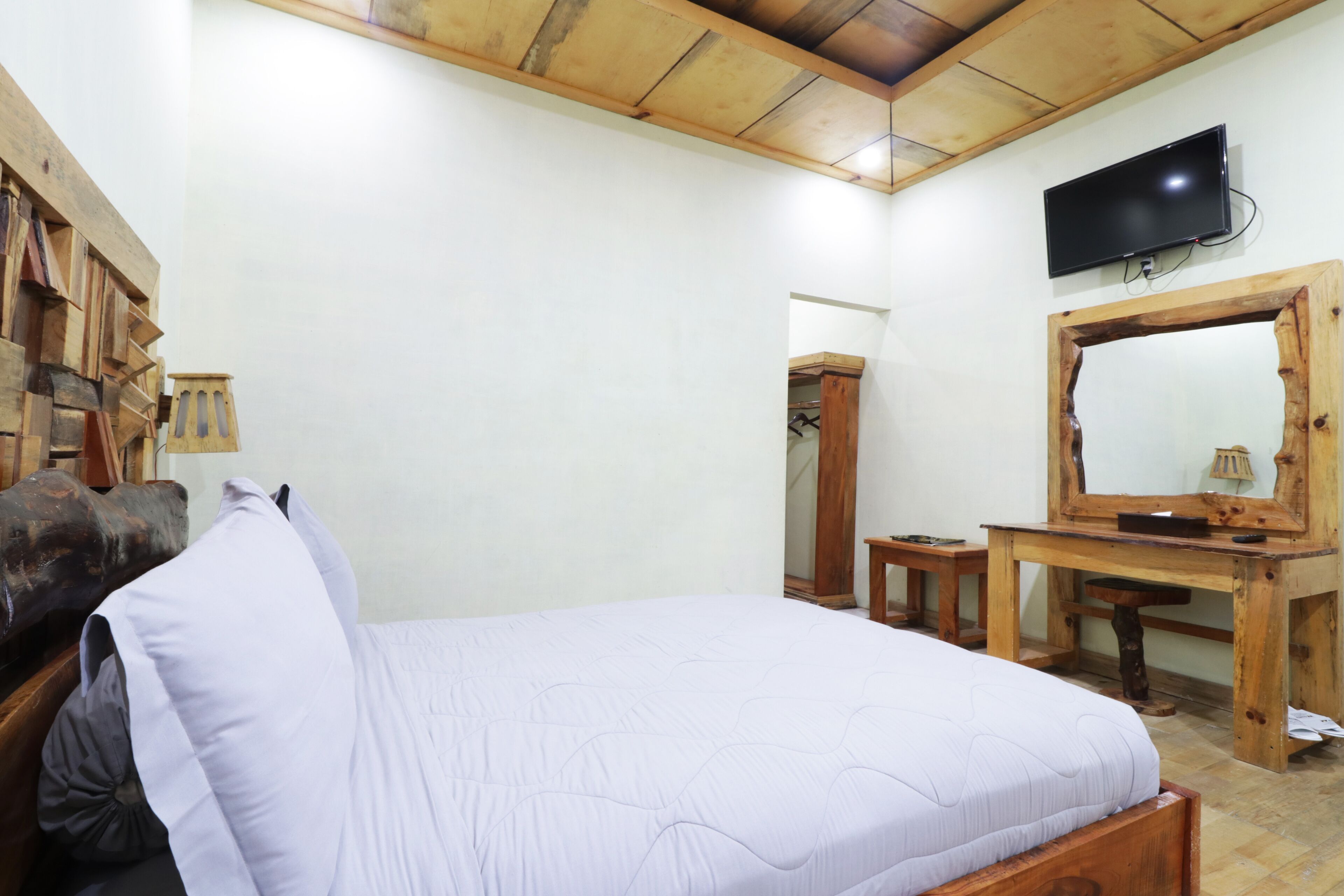 A bedroom with a bed, wooden desk, and a television mounted on the wall.