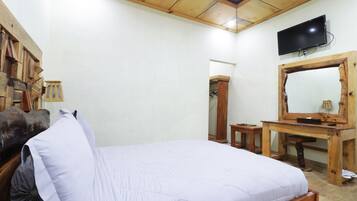 Quarto com cama, escrivaninha de madeira e televisão fixada na parede.