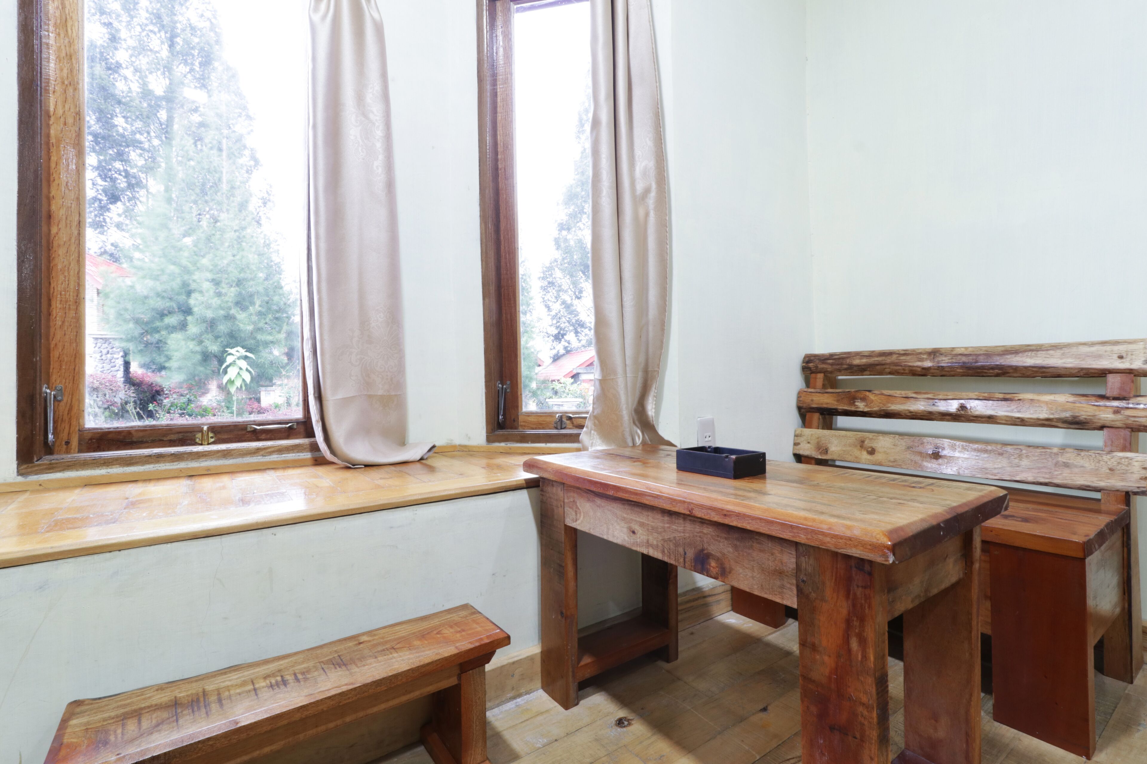 Una habitación pequeña y rústica con un banco de madera, una mesita y una ventana con cortinas.