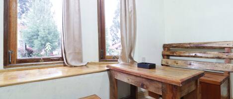 Una habitación pequeña y rústica con un banco de madera, una mesita y una ventana con cortinas.