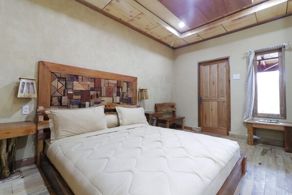 A bedroom with a wooden headboard, a large bed, a wooden desk, and a window with curtains.