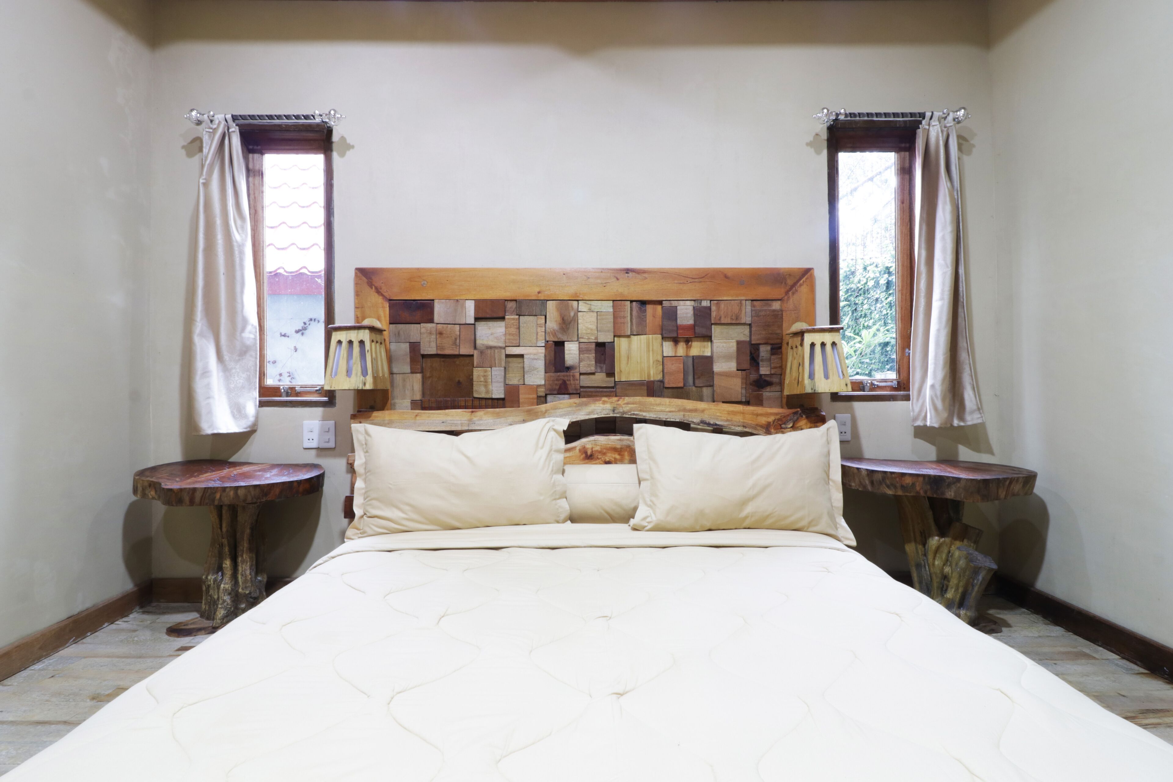 Un dormitorio con cabecera de madera, cama con ropa de cama blanca, dos mesitas de noche y cortinas en las ventanas.