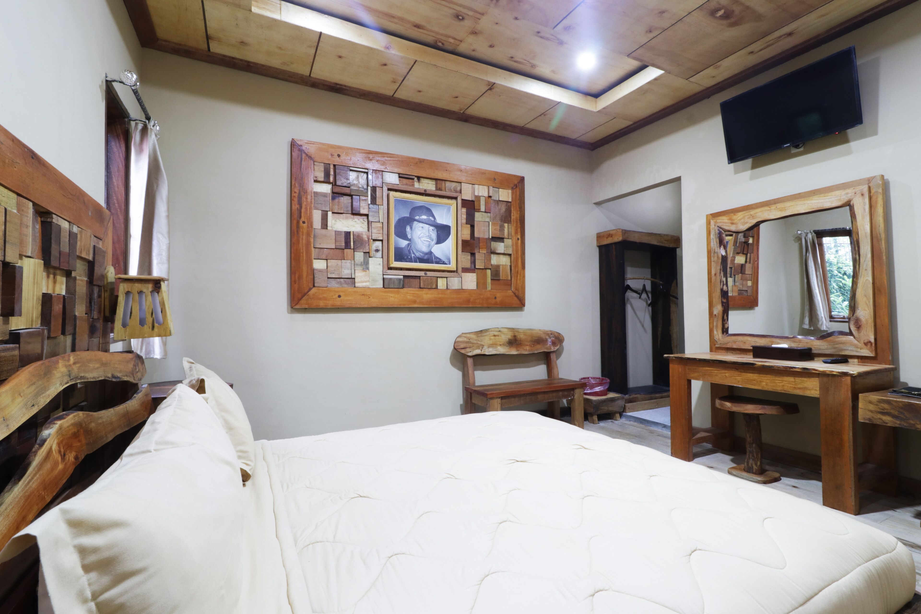 Un dormitorio con cabecera de madera, una cama grande, cómoda de madera, un espejo y un televisor montado en la pared.