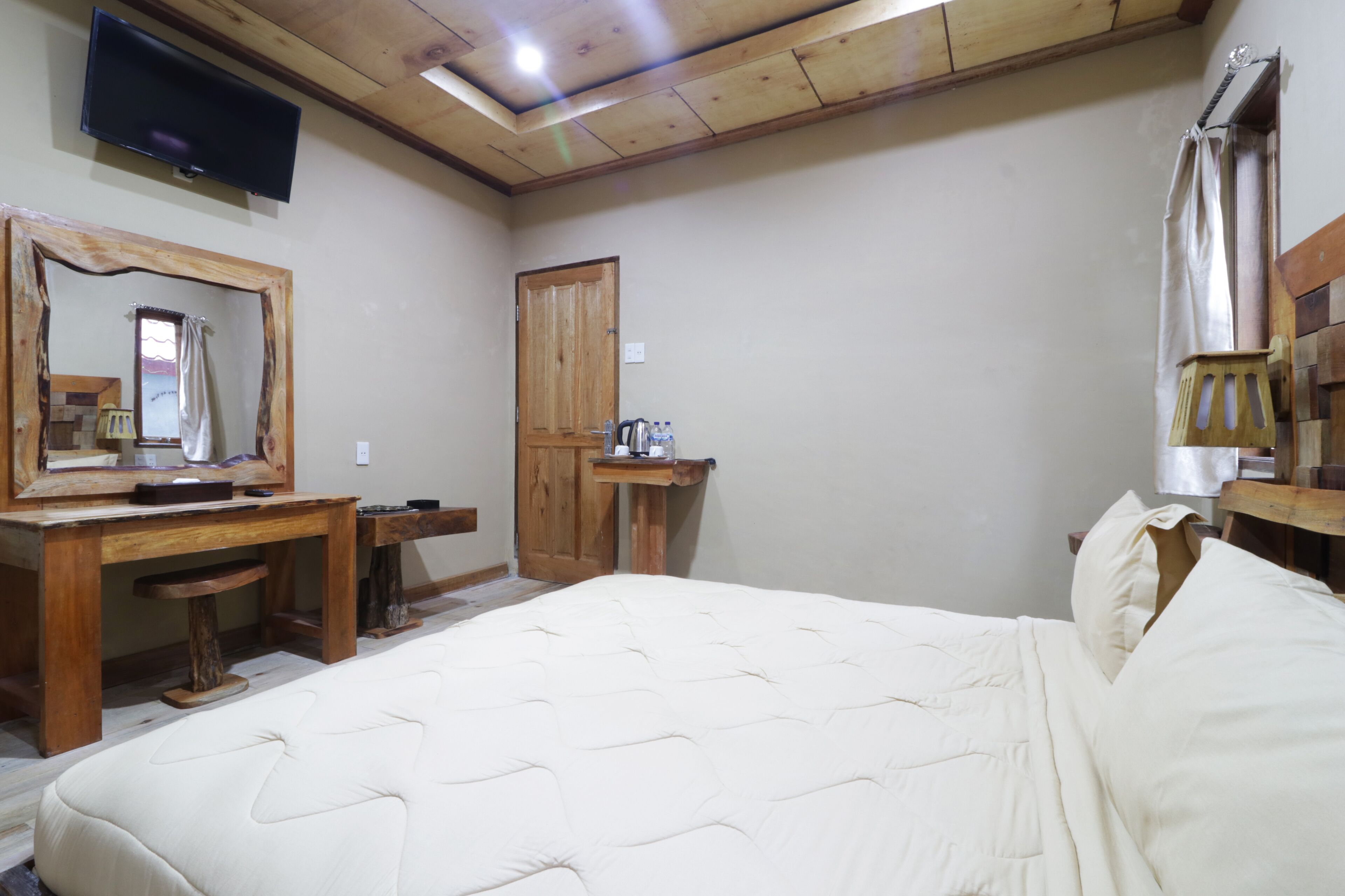 Quarto com cama grande, escrivaninha de madeira e TV fixada na parede.