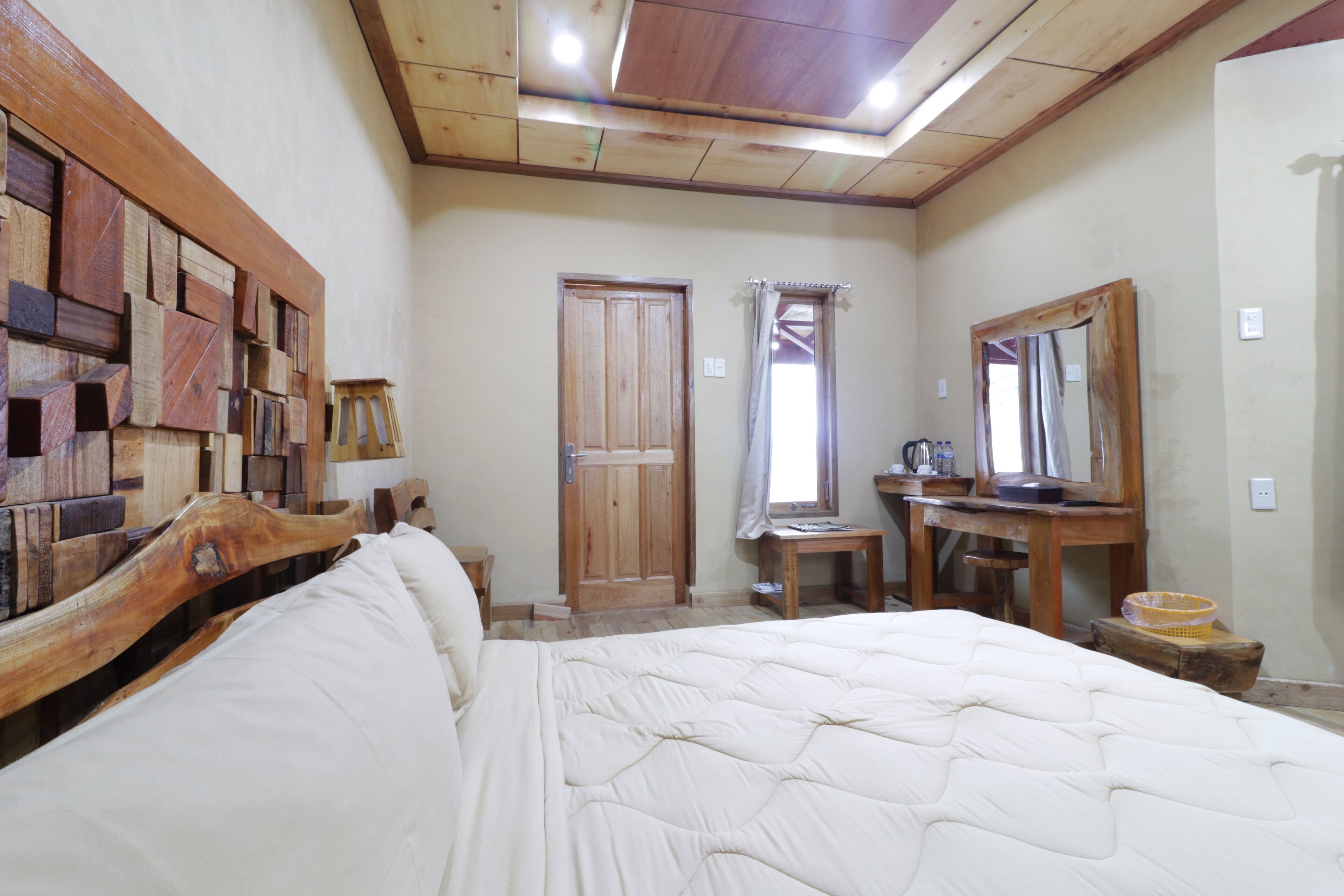 A bedroom with a wooden headboard, a large bed, a wooden dresser, a mirror, and a door.
