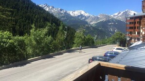 Eine Straße mit parkenden Autos am Rand, ein Fußgänger und ein Gebirge im Hintergrund.