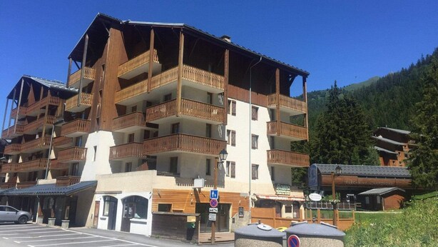 Ein mehrstöckiges Hotel mit hölzernen Balkonen und einem Skiort im Hintergrund.