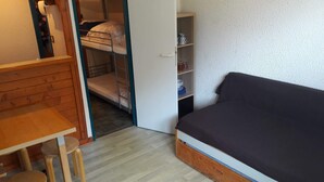 Ein kleines Zimmer mit Etagenbett, einem Einzelbett, einem Holztisch und einem Regal mit Geschirr.