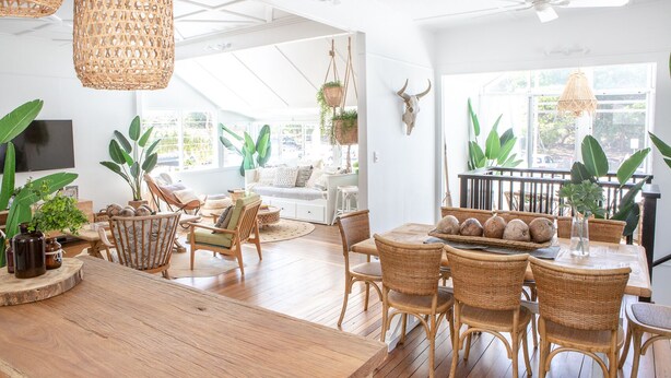 A spacious living area with a wooden dining table, wicker chairs, and a large window providing natural light.