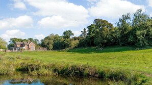 Une grande maison avec un jardin clos et un étang.