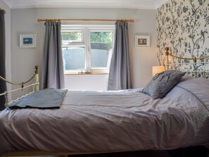 Un dormitorio con cama, cortinas, una ventana y una pared con estampado floral.