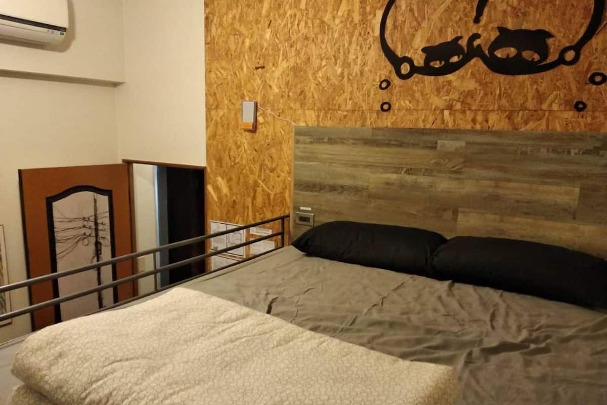A bedroom with a bed, two pillows, a headboard, a wooden wall, and a small shelf.