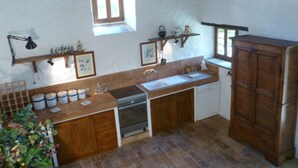 A compact kitchen with wooden cabinets, a stove, a sink, and a window. - Della Genga (Spoleto)