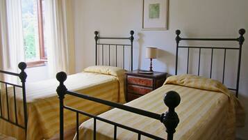 A room with two single beds with metal frames, a nightstand with a lamp, and a framed picture on the wall.