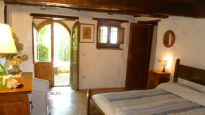 A bedroom with a bed, a wooden headboard, a nightstand with a lamp, a dresser, and a door leading to a balcony. - Della Genga (Spoleto)