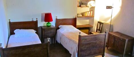 Une chambre traditionnelle avec deux lits en bois, une petite table, une chaise et une étagère remplie de livres.