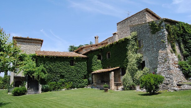 A stone building with ivy-covered walls and a tiled roof, surrounded by a well-maintained lawn. - Della Genga (Spoleto)