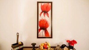 Une pièce dans laquelle on peut voir un tableau encadré représentant des fleurs rouges, un bol décoratif rempli de fruits, une petite statue et un vase contenant des fleurs rouges, le tout posé sur une table.