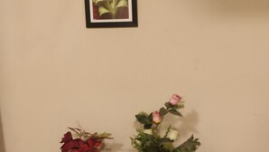 Un mur orné d’un tableau représentant des fleurs blanches, un meuble en bois foncé doté de tiroirs et deux plantes en pot, elles aussi fleuries.
