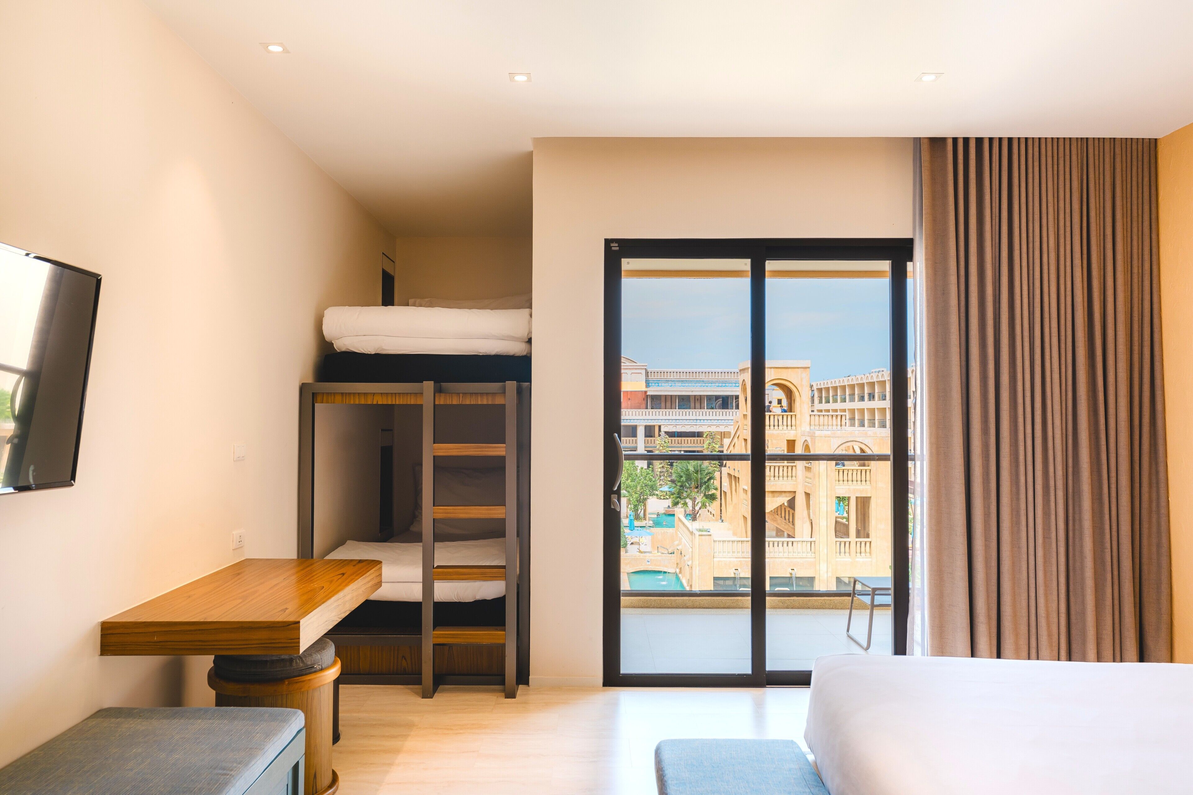 Habitación de hotel con literas, un escritorio, una ventana con vistas a edificios y una cortina.