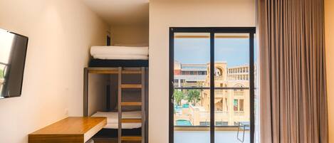 Habitación de hotel con literas, un escritorio, una ventana con vistas a edificios y una cortina.