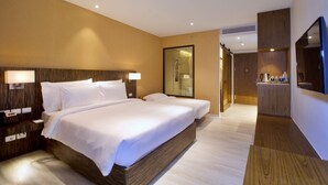 Une chambre d’hôtel moderne, dotée d’un grand lit, de tables de chevet, d’un miroir et d’une salle de bain visible à travers une porte en verre.