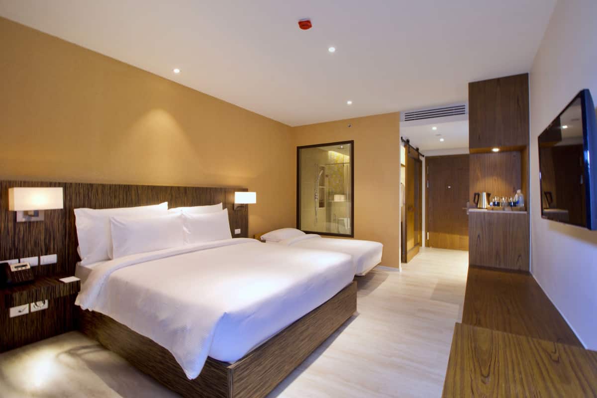 Ein modernes Hotelzimmer mit einem großen Bett, Nachttischen, einem Spiegel und einem durch eine Glastür einsehbaren Badezimmer.