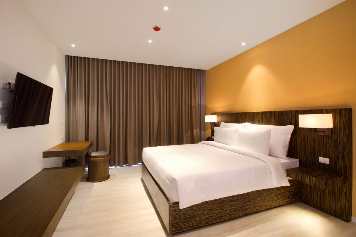 Ein modernes Hotelzimmer mit einem großen Bett, einem Nachttisch, einem an der Wand montierten Fernseher und einem Vorhang.