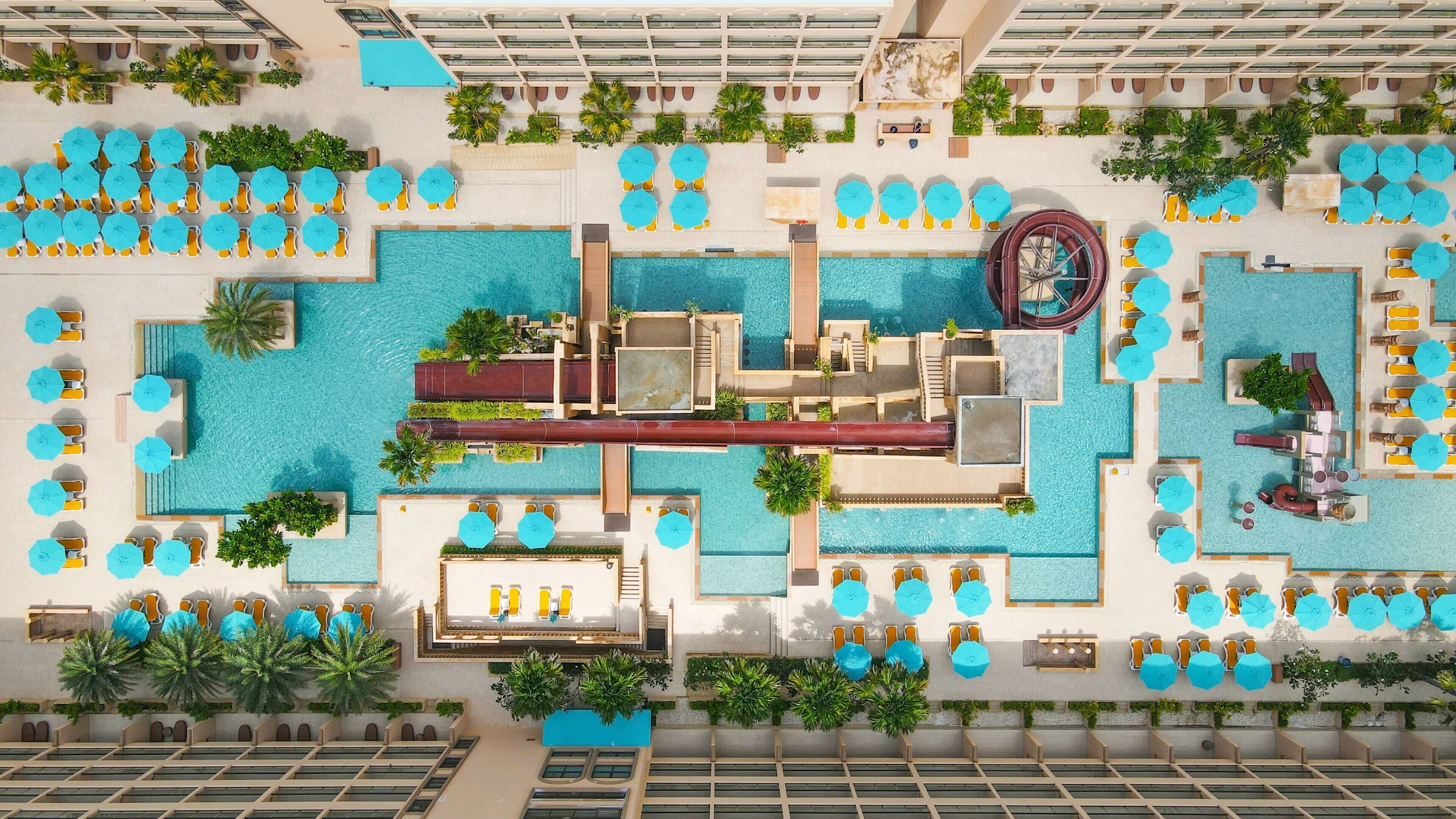 A rooftop pool area with multiple swimming pools, sun loungers, and umbrellas.