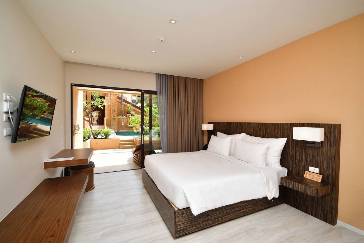 Ein modernes Hotelzimmer mit einem großen Bett, einem Holztisch, einem Fernseher und Blick auf einen Pool und Außenbereich.