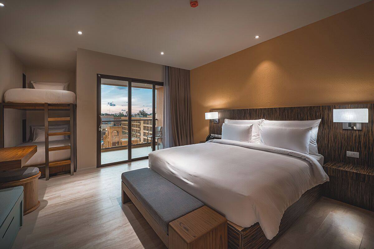 Ein modernes Hotelzimmer mit einem großen Bett, einem Schreibtisch und Blick auf die Stadt durch ein großes Fenster.
