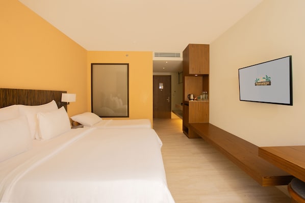 Une chambre d’hôtel avec un grand lit, une table de chevet en bois, un téléviseur fixé au mur et une porte donnant sur une autre pièce.
