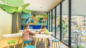 A children's play area with a colorful mural, wooden stools, and a large window offering a view of the outdoor area.