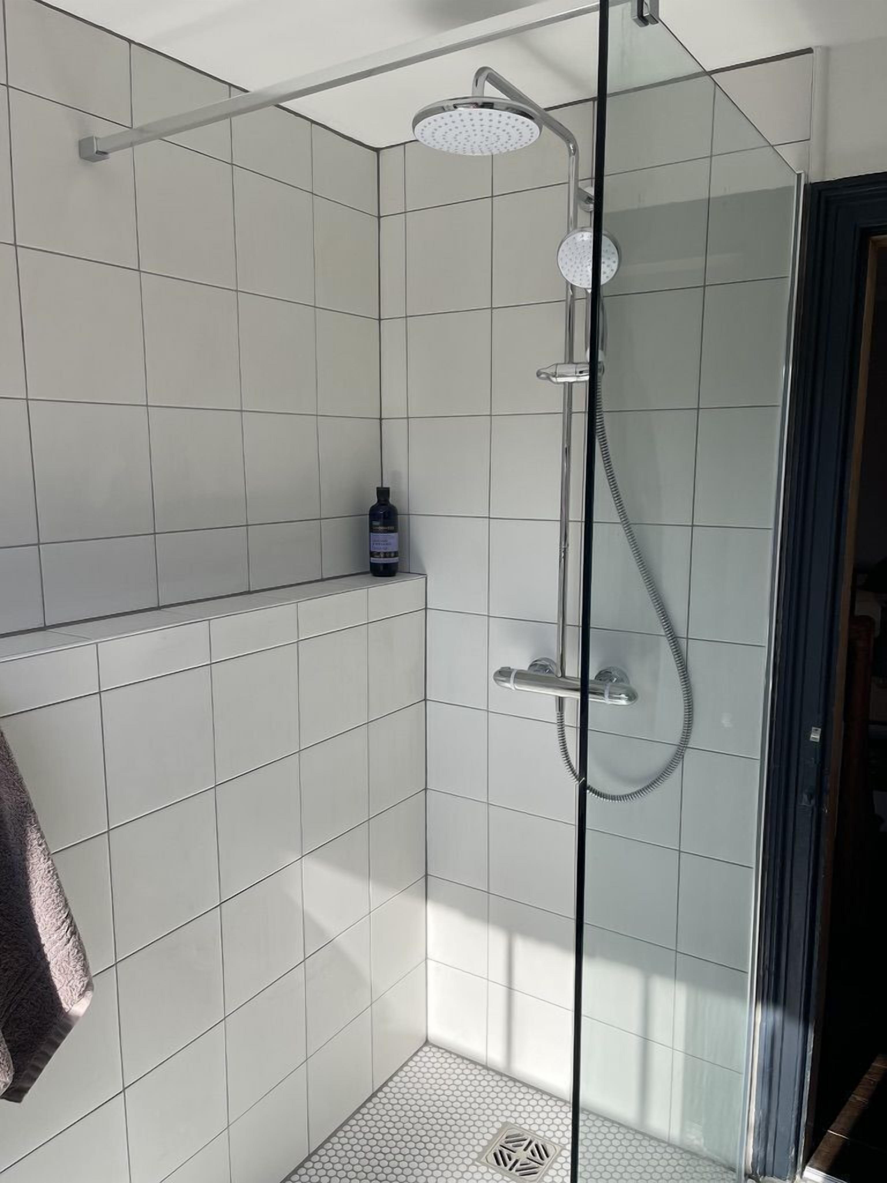 Chuveiro com divisória de vidro, chuveiro manual e torneira fixa na parede.