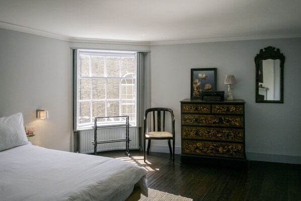 A bedroom with a large window, a wooden dresser, a chair, and a bed. - A stunning Grade II listed apartment in the heart of the conservation area. (Deal)