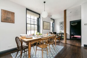 A dining area with a wooden table, chairs, and a patterned rug. There are windows with curtains, a hanging light fixture, and a wall-mounted sign. - A stunning Grade II listed apartment in the heart of the conservation area. (Deal)
