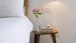 A neatly made bed with white bedding, a small wooden bedside table with a vase of flowers, a stack of books, and a wall-mounted light fixture. - A stunning Grade II listed apartment in the heart of the conservation area. (Deal)