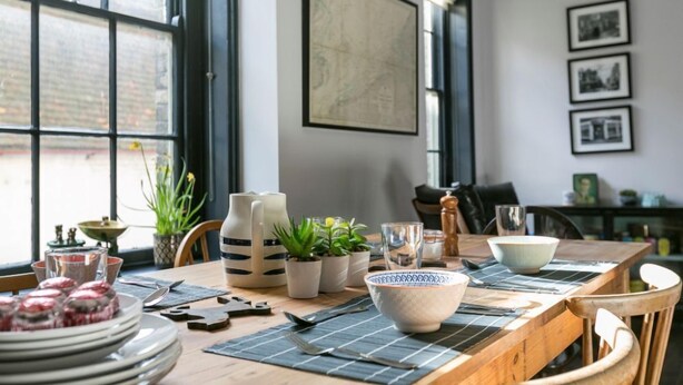 A dining area with a wooden table, potted plants, and a large window. - A stunning Grade II listed apartment in the heart of the conservation area. (Deal)