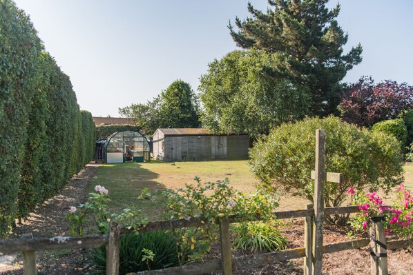 A garden with a wooden fence, a greenhouse, and a stone building.