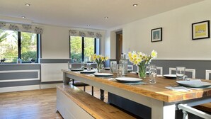 A modern kitchen with a long wooden bench, a dining table set with plates and glasses, and a vase of daffodils.